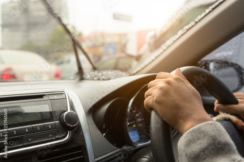 Hands of driving man while hands on the wheel in the car while it is raining heavily on the road and windshield wipers clean the window view to drive safely