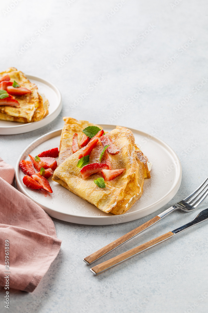 Crepes served with cream cheese and fresh strawberry on white background. 