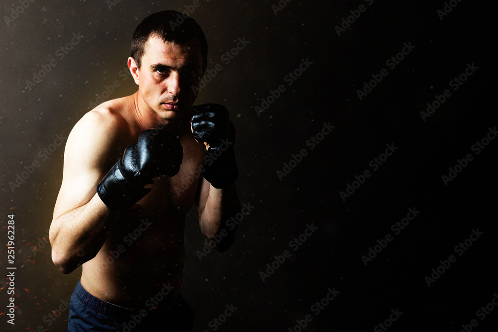 A man in gloves for fighting without rules MMA on a black background. Workout concept, combat training