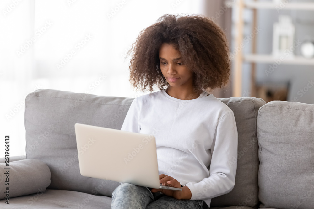 African adolescent girl sitting on couch using computer African adolescent girl sitting on couch using computer
