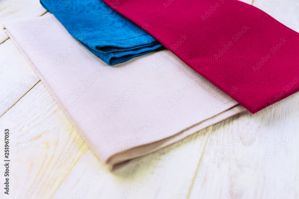 close up of cloth napkins of beige, blue and burgundy colors on rustic white wooden table.