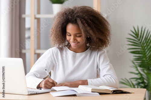 Positive african schoolgirl sitting at desk and study