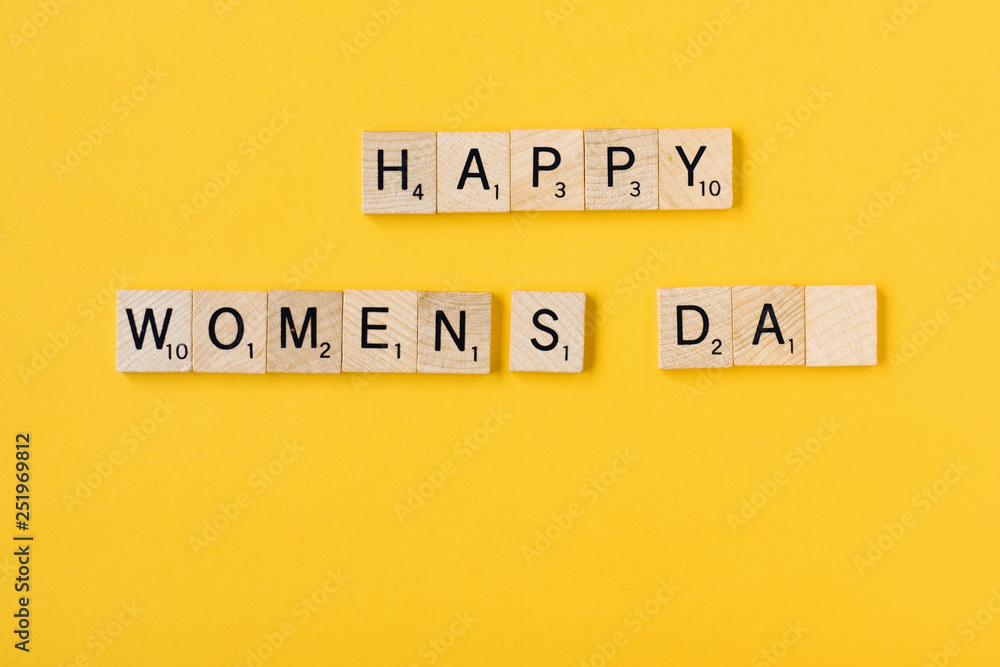 Naklejka premium Top view Message happy woomans day spelled in wooden blocks on yellow background. Love, 8 march background. Gift, greeting, compliment concept. Copy space. place for text