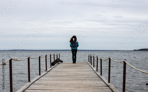 The girl stands with her back on the pier and looks into the distance in cloudy weather
