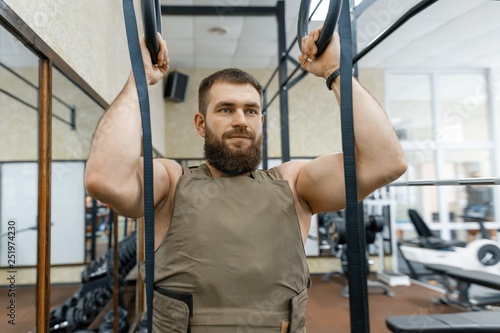 Military sport, muscular caucasian bearded adult man doing exercises in the gym dressed in a bulletproof armored vest