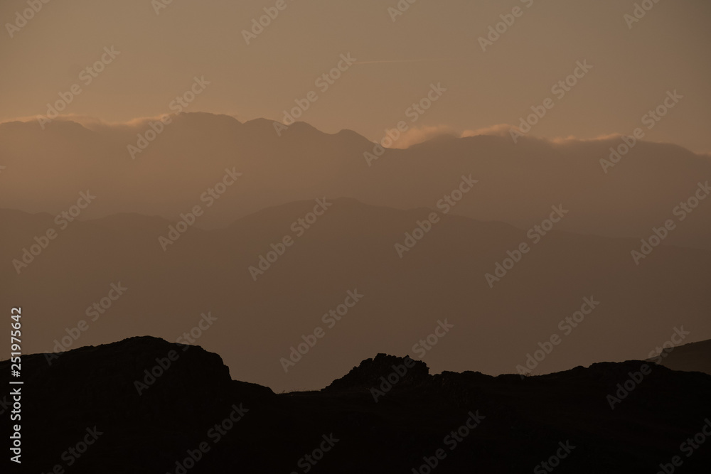 A silhouette of Crinkle Crags skyline created by evening light, seen from Loughrigg Fell, Lake District, UK A silhouette of Crinkle Crags skyline created by evening light, seen from Loughrigg Fell, Lake District, UK