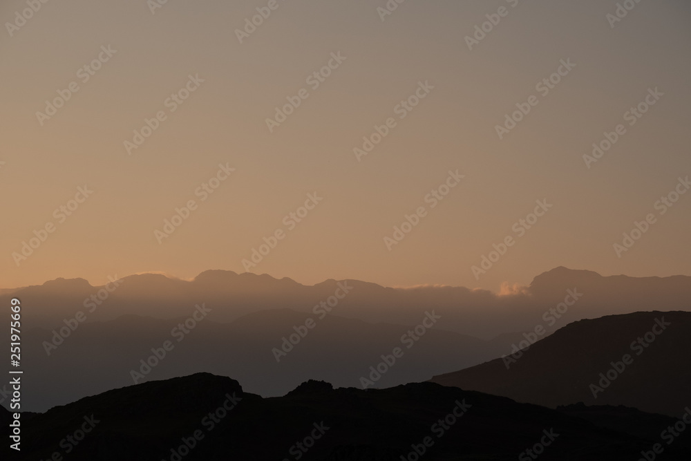 A silhouette of Crinkle Crags and Bowfell created by evening light, seen from Loughrigg Fell, Lake District, UK