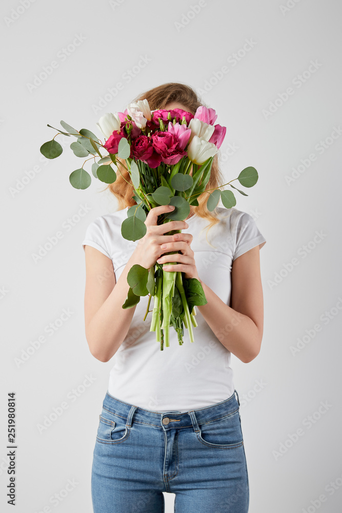 girl holding fresh bouquet with tulips, eucalyptus and roses in front of face isolated on grey girl holding fresh bouquet with tulips, eucalyptus and roses in front of face isolated on grey