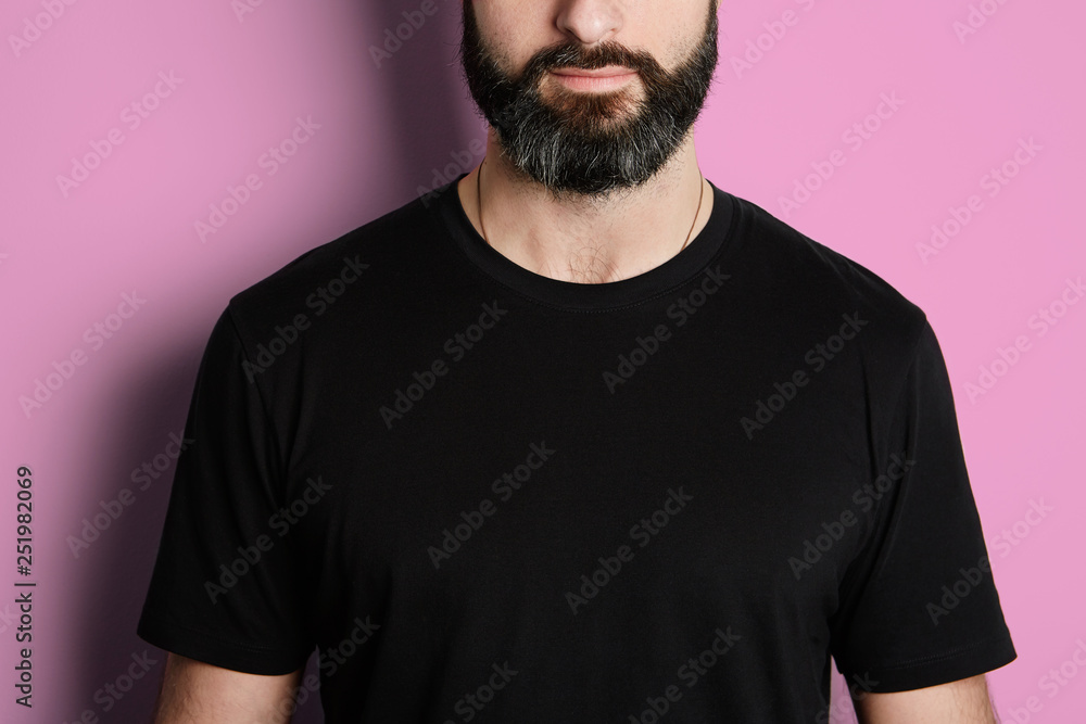 Obraz premium Portrait of bearded man in black tshirt on the empty pink background.