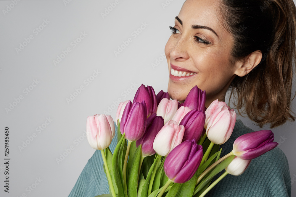 Closeup portrait of a smiling young woman holding colored tulips bouquet isolated over gray background. Closeup portrait of a smiling young woman holding colored tulips bouquet isolated over gray background.