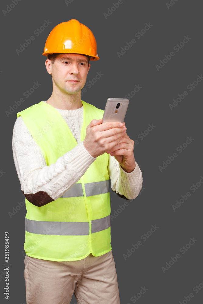the man in a helmet with phone, in a vest looks in phone the man in a helmet with phone, in a vest looks in phone