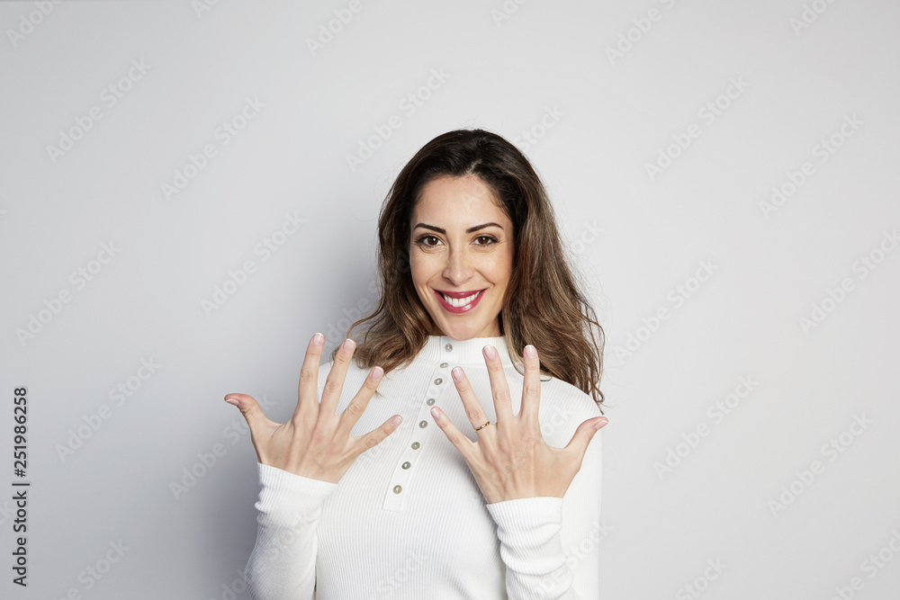 Handsome positive woman in white shirt looking at camera and showing hands gesture while standing isolated on gray background Handsome positive woman in white shirt looking at camera and showing hands gesture while standing isolated on gray background