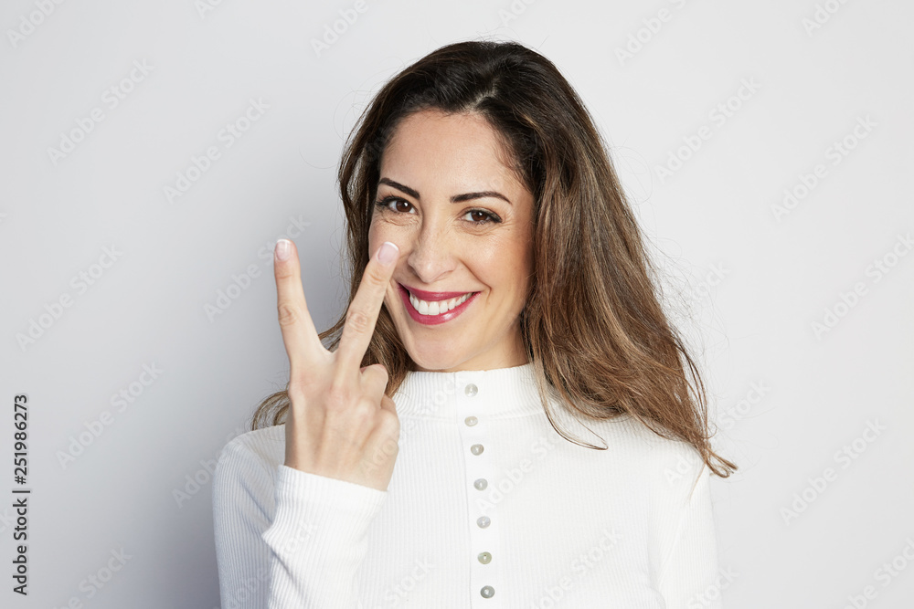 Handsome positive woman in white shirt looking at camera and showing hands gesture while standing isolated on gray background Handsome positive woman in white shirt looking at camera and showing hands gesture while standing isolated on gray background