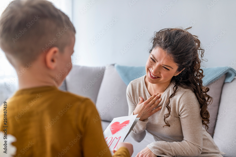Happy mother's day! Child boy congratulates mom and gives her flowers and postcard. Mum and boy smiling and hugging. Family holiday and togetherness. Happy mother's day! Child boy congratulates mom and gives her flowers and postcard. Mum and boy smiling and hugging. Family holiday and togetherness.