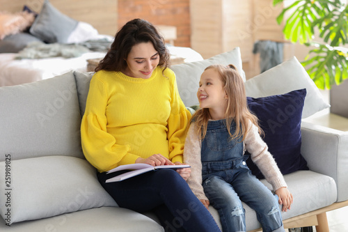 Pregnant mother with little daughter reading book at home