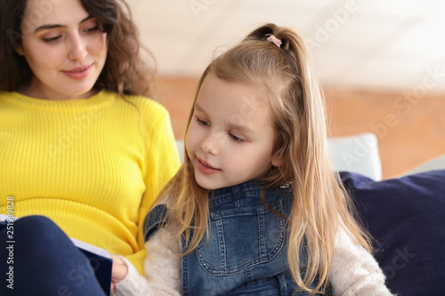 Pregnant mother with little daughter reading book at home