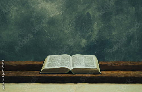 Open Bible on a old table. Beautiful gray wall background. Religion concept. photo