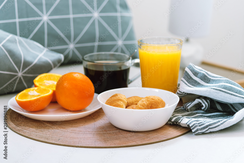 Morning breakfast in bed, hotel room. Croissants, black coffee, oranges and juice on the wooden tray. Morning breakfast in bed, hotel room. Croissants, black coffee, oranges and juice on the wooden tray.