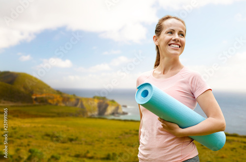 fitness  sport and healthy lifestyle concept - happy smiling woman with exercise mat over big sur coast of california background