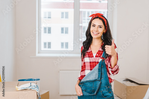 Cheerful woman showing thumb up while standing at home