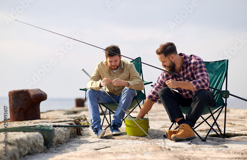 leisure and people concept - friends or fishermen adjusting fishing rods with bait on pier