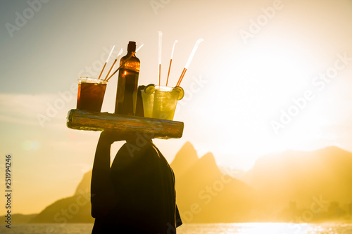 Scenic sunset view of Two Brothers Mountain with an unrecognizable silhouette of a beach vendor carrying caipirinha cocktails passing in silhouette at Arpoador in Rio de Janeiro, Brazil photo