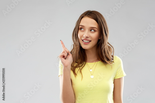 people concept - smiling young woman or teenage girl in blank yellow t-shirt pointing finger up over grey background photo