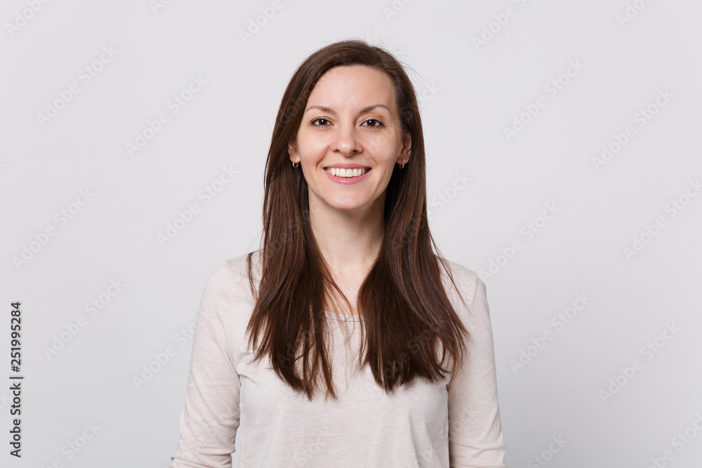 Portrait of smiling attractive young woman in light clothes standing and looking camera isolated on white wall background in studio. People sincere emotions, lifestyle concept. Mock up copy space. Portrait of smiling attractive young woman in light clothes standing and looking camera isolated on white wall background in studio. People sincere emotions, lifestyle concept. Mock up copy space.