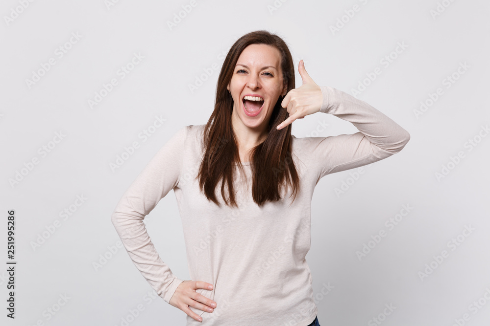 Cheerful young woman in light clothes keeping mouth wide open, doing phone gesture like says call me back isolated on white background. People sincere emotions, lifestyle concept. Mock up copy space. Cheerful young woman in light clothes keeping mouth wide open, doing phone gesture like says call me back isolated on white background. People sincere emotions, lifestyle concept. Mock up copy space.