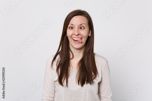 ?razy funny young woman with beveled eyes in light clothes showing tongue, fooling around isolated on white wall background in studio. People sincere emotions, lifestyle concept. Mock up copy space.