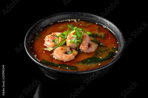 Hot miso soup with shrimp, seaweed, mushrooms, herbs in bowl on black background. Japanese food.