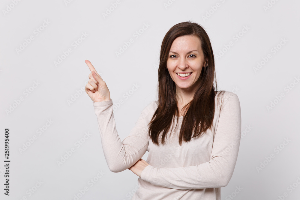 Portrait of smiling attractive young woman in light clothes pointing index finger aside up isolated on white wall background in studio. People sincere emotions, lifestyle concept. Mock up copy space. Portrait of smiling attractive young woman in light clothes pointing index finger aside up isolated on white wall background in studio. People sincere emotions, lifestyle concept. Mock up copy space.
