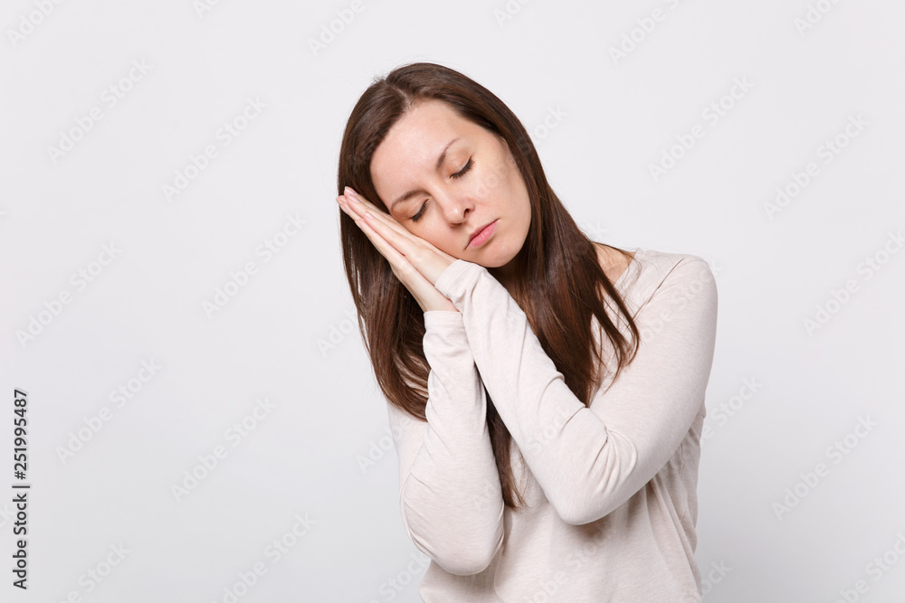Portrait of relaxed young woman in light clothes keeping eyes closed, sleeping with hands near face isolated on white wall background. People sincere emotions, lifestyle concept. Mock up copy space. Portrait of relaxed young woman in light clothes keeping eyes closed, sleeping with hands near face isolated on white wall background. People sincere emotions, lifestyle concept. Mock up copy space.