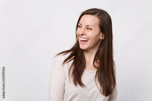Portrait of laughing joyful attractive young woman in light clothes standing, looking aside isolated on white wall background in studio. People sincere emotions lifestyle concept. Mock up copy space.