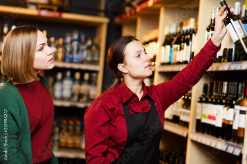 Photo of seller and buyer on blurred background of racks with bottles of wine