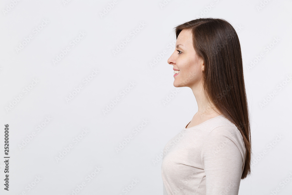 Side view of smiling attractive beautiful brunette young woman in light clothes standing isolated on white wall background in studio. People sincere emotions lifestyle concept. Mock up copy space. Side view of smiling attractive beautiful brunette young woman in light clothes standing isolated on white wall background in studio. People sincere emotions lifestyle concept. Mock up copy space.