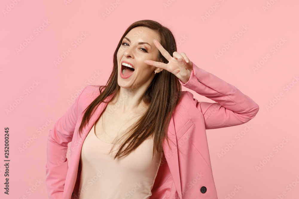Cheerful funny young woman in jacket keeping mouth wide open, showing victory gesture isolated on pastel pink wall background in studio. People sincere emotions, lifestyle concept. Mock up copy space. Cheerful funny young woman in jacket keeping mouth wide open, showing victory gesture isolated on pastel pink wall background in studio. People sincere emotions, lifestyle concept. Mock up copy space.