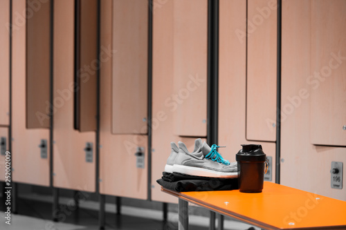 Close up of sports shoes, sportswear and sport water bottle in gym locker room.