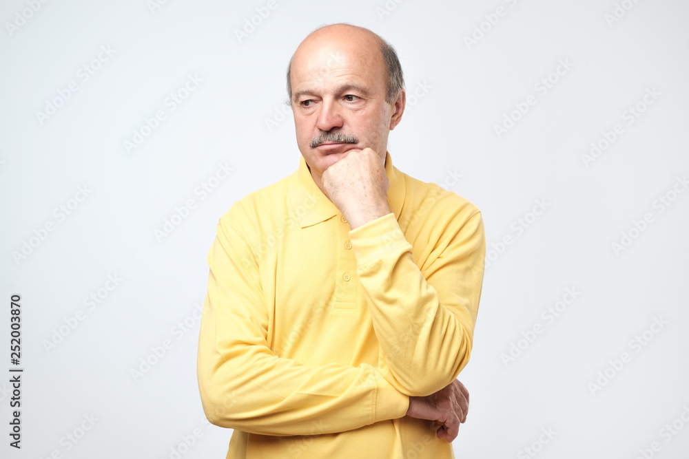 Portrait of casual mature man in yellow shirt thinking and looking puzzled. Portrait of casual mature man in yellow shirt thinking and looking puzzled.
