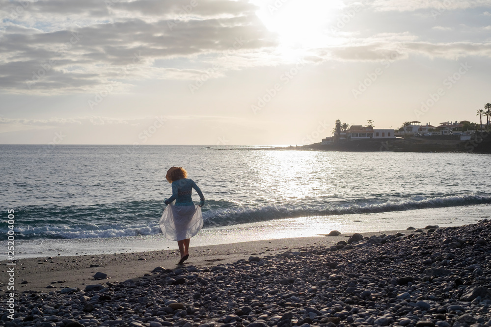 Girl viewed from rear dancing at the beach with ocean in background - vacation and happiness concept for people love freedom and nature Girl viewed from rear dancing at the beach with ocean in background - vacation and happiness concept for people love freedom and nature