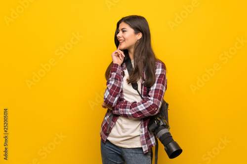 Photographer teenager girl over yellow wall thinking an idea while looking up