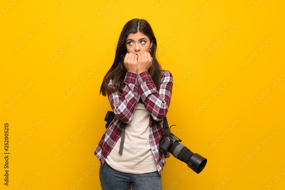 Photographer teenager girl over yellow wall nervous and scared putting hands to mouth Photographer teenager girl over yellow wall nervous and scared putting hands to mouth
