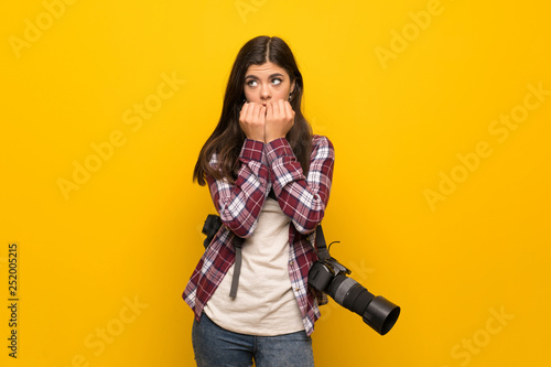 Photographer teenager girl over yellow wall nervous and scared putting hands to mouth