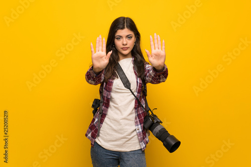 Photographer teenager girl over yellow wall making stop gesture and disappointed