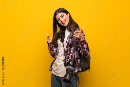 Photographer teenager girl over yellow wall pointing to the front and smiling © luismolinero
