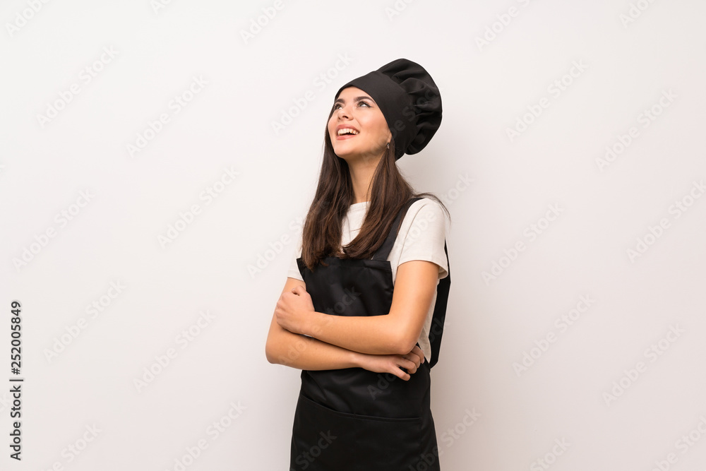 Teenager chef over white wall looking up while smiling Teenager chef over white wall looking up while smiling