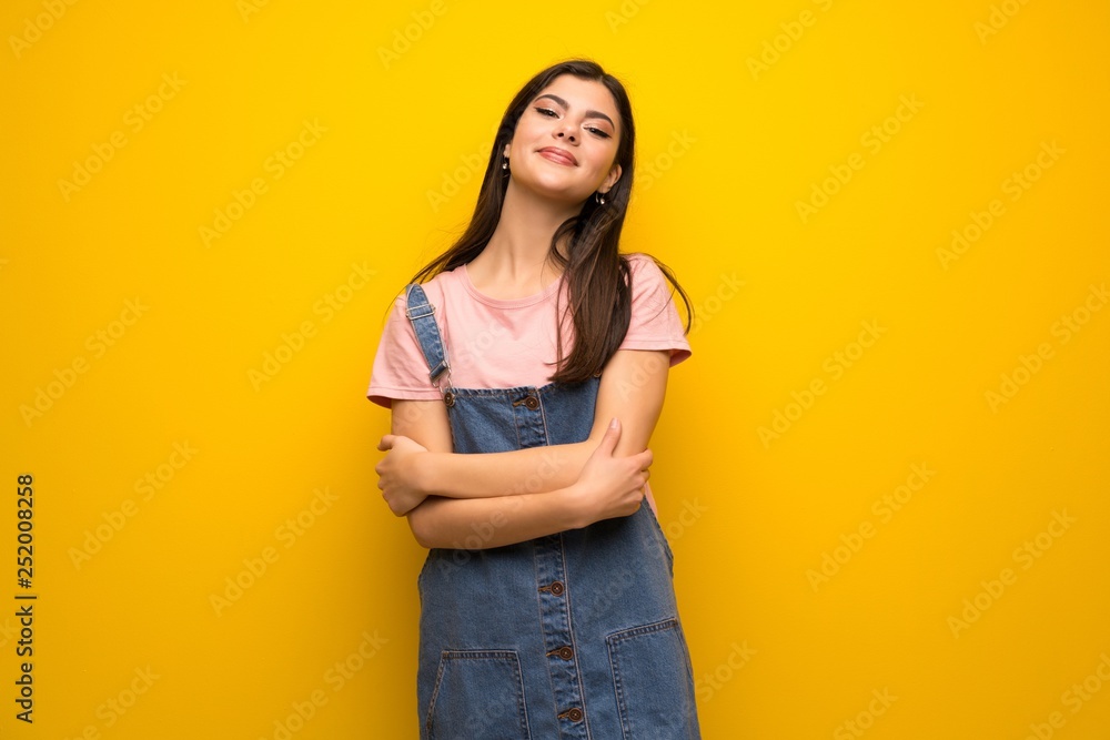 Teenager girl over yellow wall keeping the arms crossed in frontal position Teenager girl over yellow wall keeping the arms crossed in frontal position