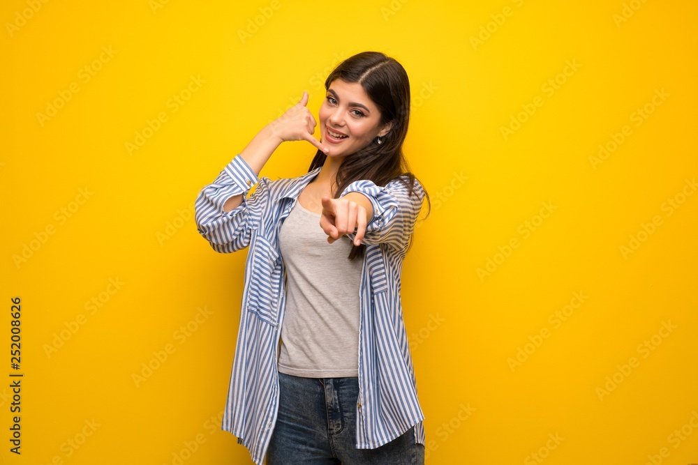 Teenager girl over yellow wall making phone gesture and pointing front Teenager girl over yellow wall making phone gesture and pointing front