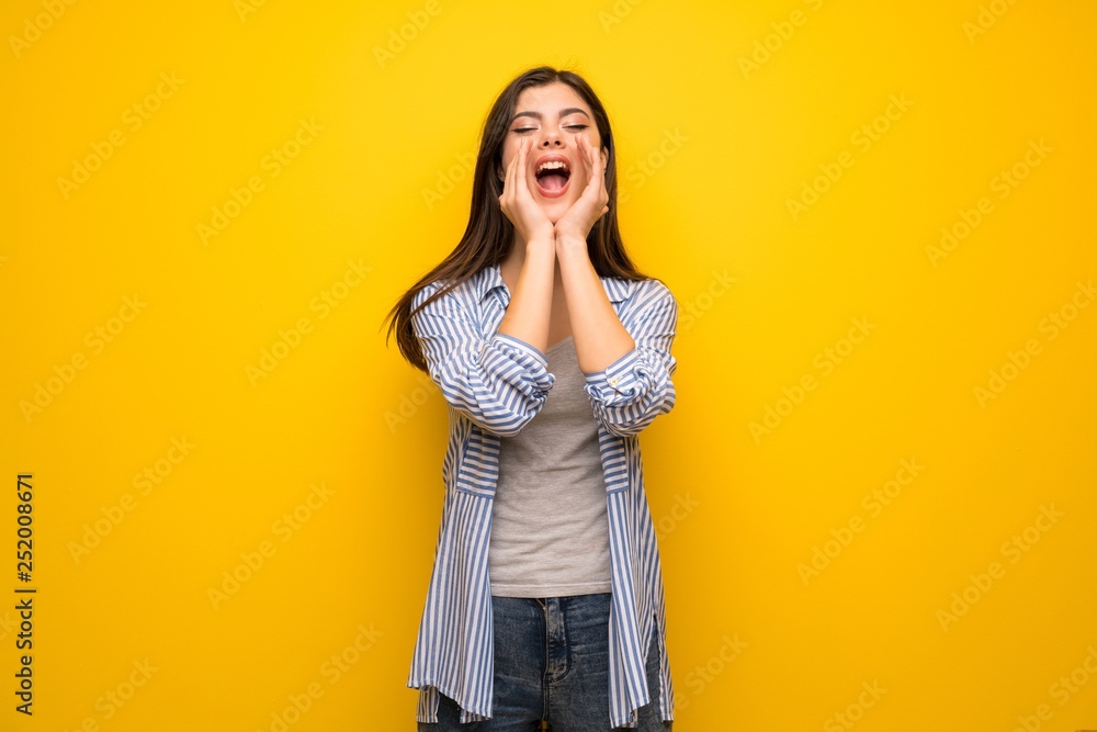 Teenager girl over yellow wall shouting and announcing something Teenager girl over yellow wall shouting and announcing something