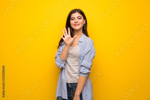 Teenager girl over yellow wall counting five with fingers
